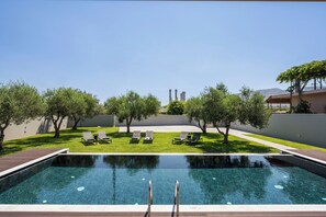 Une piscine entourée de chaises longues et d’arbres, dans un espace paysager aménagé.
