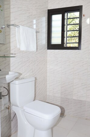 A bathroom with a toilet, sink, and a window with a view of greenery. - Casa Hôtel Résidence (Abidjan)