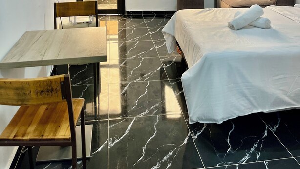 A hotel room with a bed, a desk with a chair, a TV mounted on the wall, and two windows providing a view of greenery. - Casa Hôtel Résidence (Abidjan)