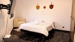 A hotel room with a bed, a sofa, a flat-screen TV mounted on the wall, and a wooden wardrobe. - Casa Hôtel Résidence (Abidjan)