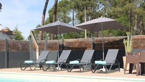 A poolside area with lounge chairs and umbrellas. - Au Bon Coin du Lac (Mimizan)
