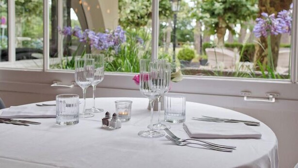 A table set for dining with clear glassware and a view of a garden through a window. - Au Bon Coin du Lac (Mimizan)
