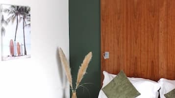 Un lit bien fait, recouvert d’une couverture verte, avec une tête de lit en bois et une petite table de chevet ornée d’un vase contenant des plumes d’herbe des pampas.