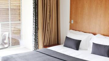 Een hotelkamer met een bed, een houten hoofdbord en een raam met luxaflex.