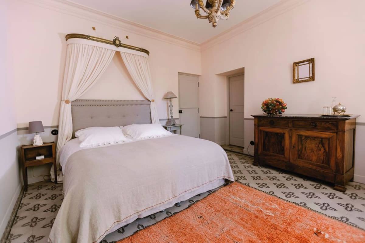 Une chambre à coucher avec un lit à baldaquin, une commode en bois, une table de chevet et un tapis à motifs.
