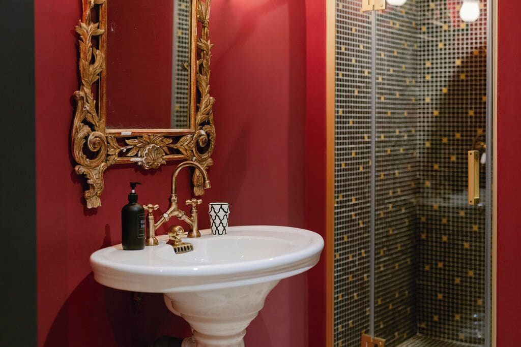 A bathroom with a white pedestal sink, gold faucets, and a gold-framed mirror.