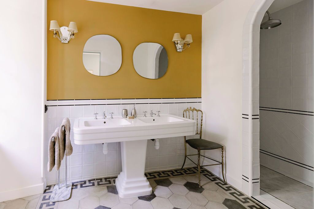A bathroom with a white pedestal sink, two wall-mounted mirrors, and a shower area.