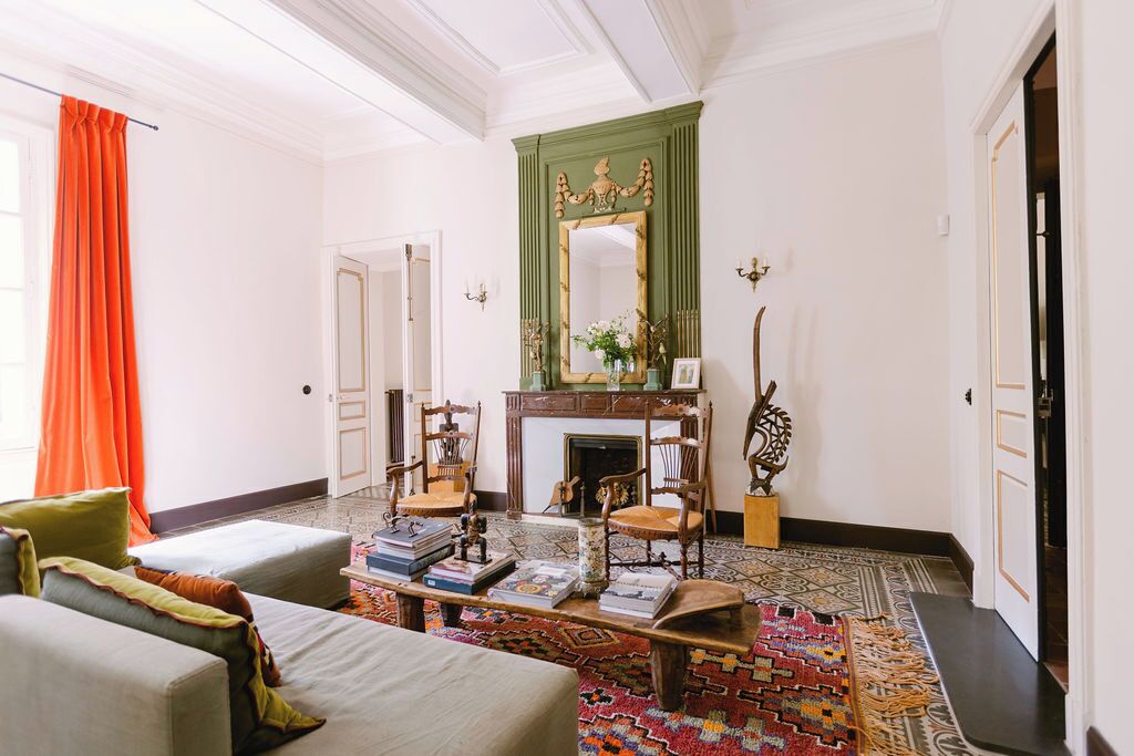 A room with a fireplace, two armchairs, a coffee table with books, and a patterned rug.