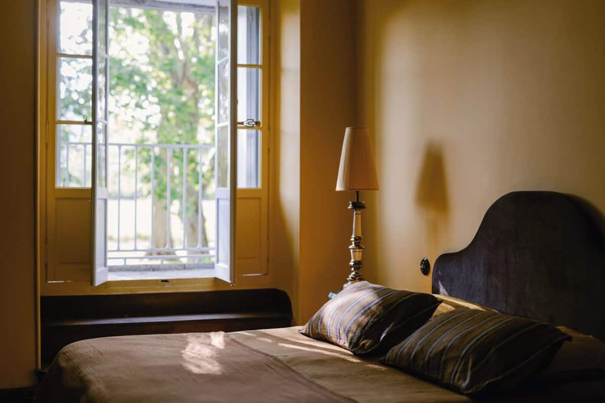 Une chambre à coucher avec un lit, une fenêtre donnant sur un paysage verdoyant et une lampe de chevet.
