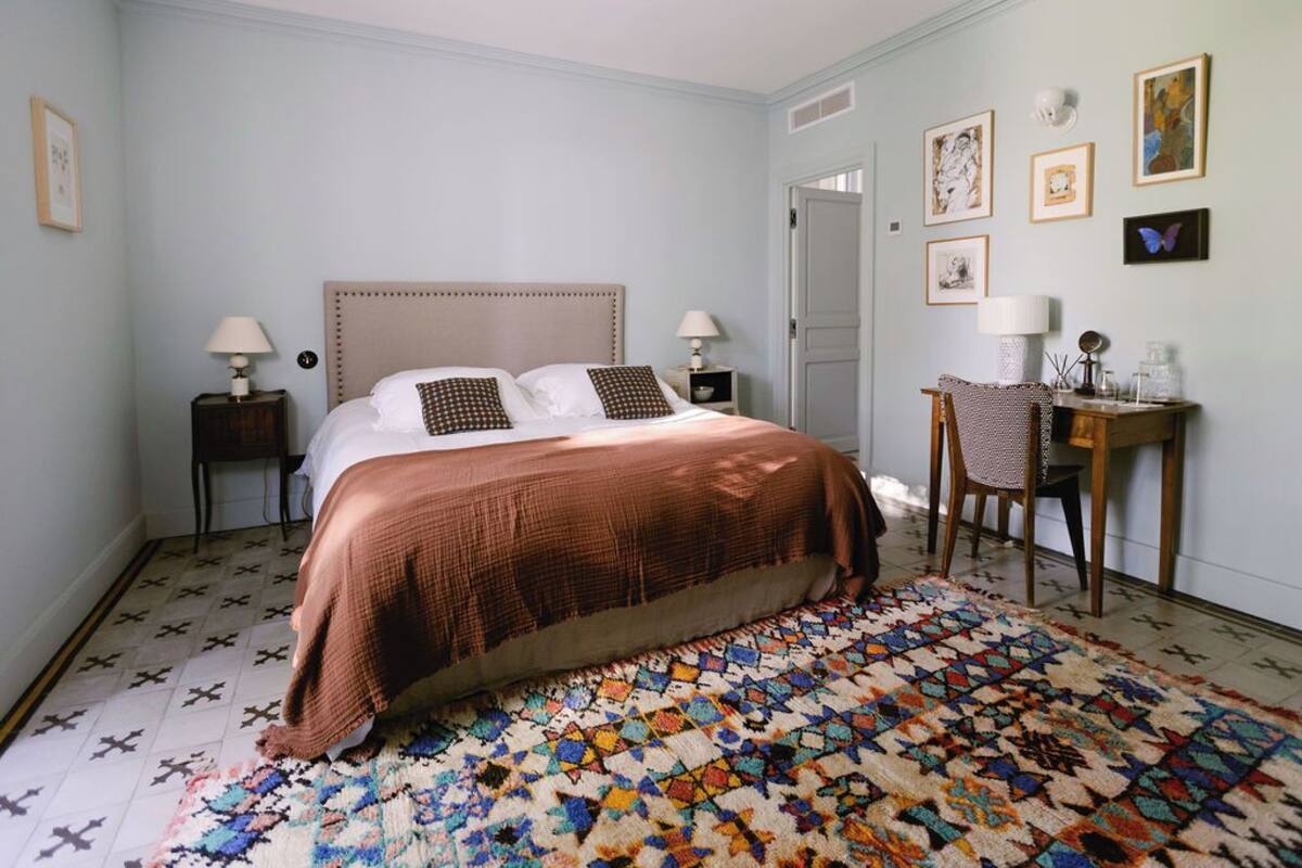 Une chambre à coucher comprenant un lit, deux tables de chevet avec des lampes, une chaise et un bureau avec une lampe.
