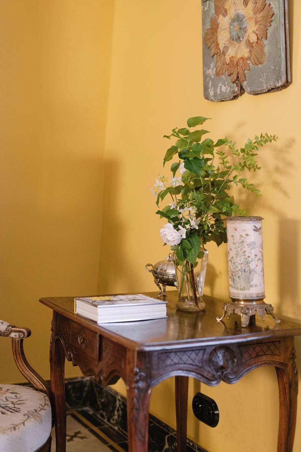 Een houten tafel met een boek, een vaas met bloemen en een decoratieve lamp.