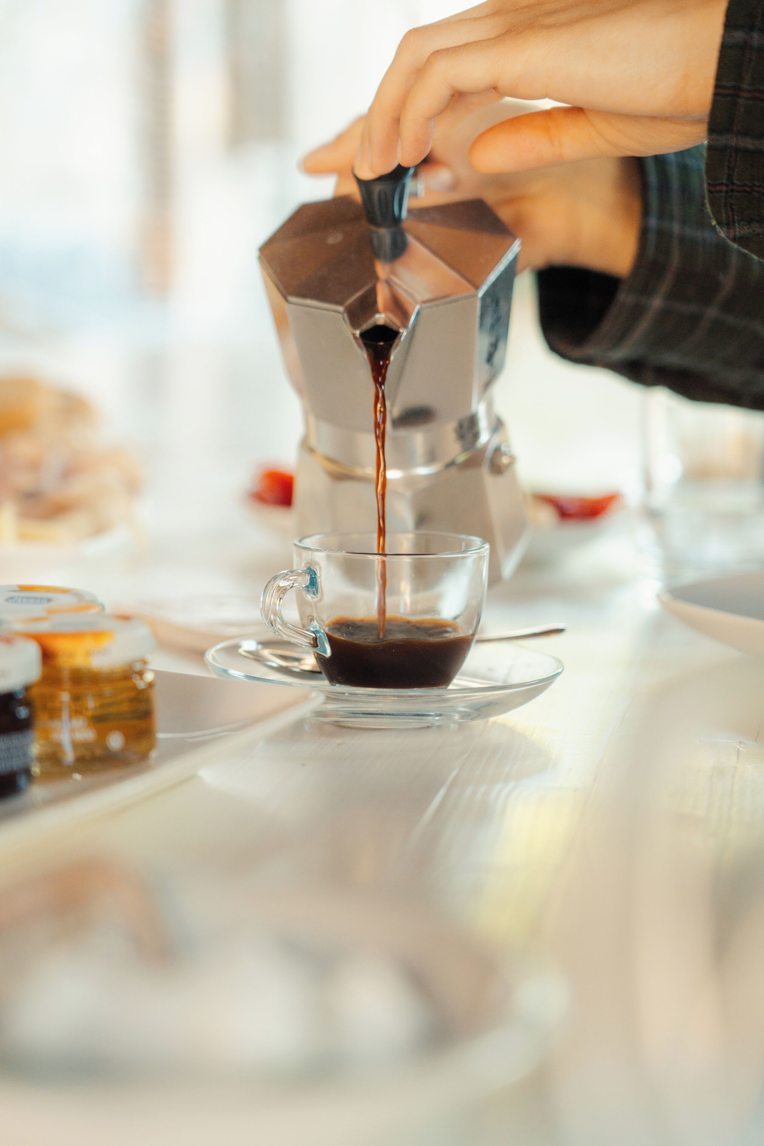 Una persona serviendo café en un vaso transparente sobre una mesa.