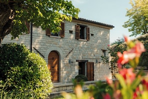 A stone building with arched windows and shutters, surrounded by greenery. - Le Fontanelle Country House (Sant'Ippolito)
