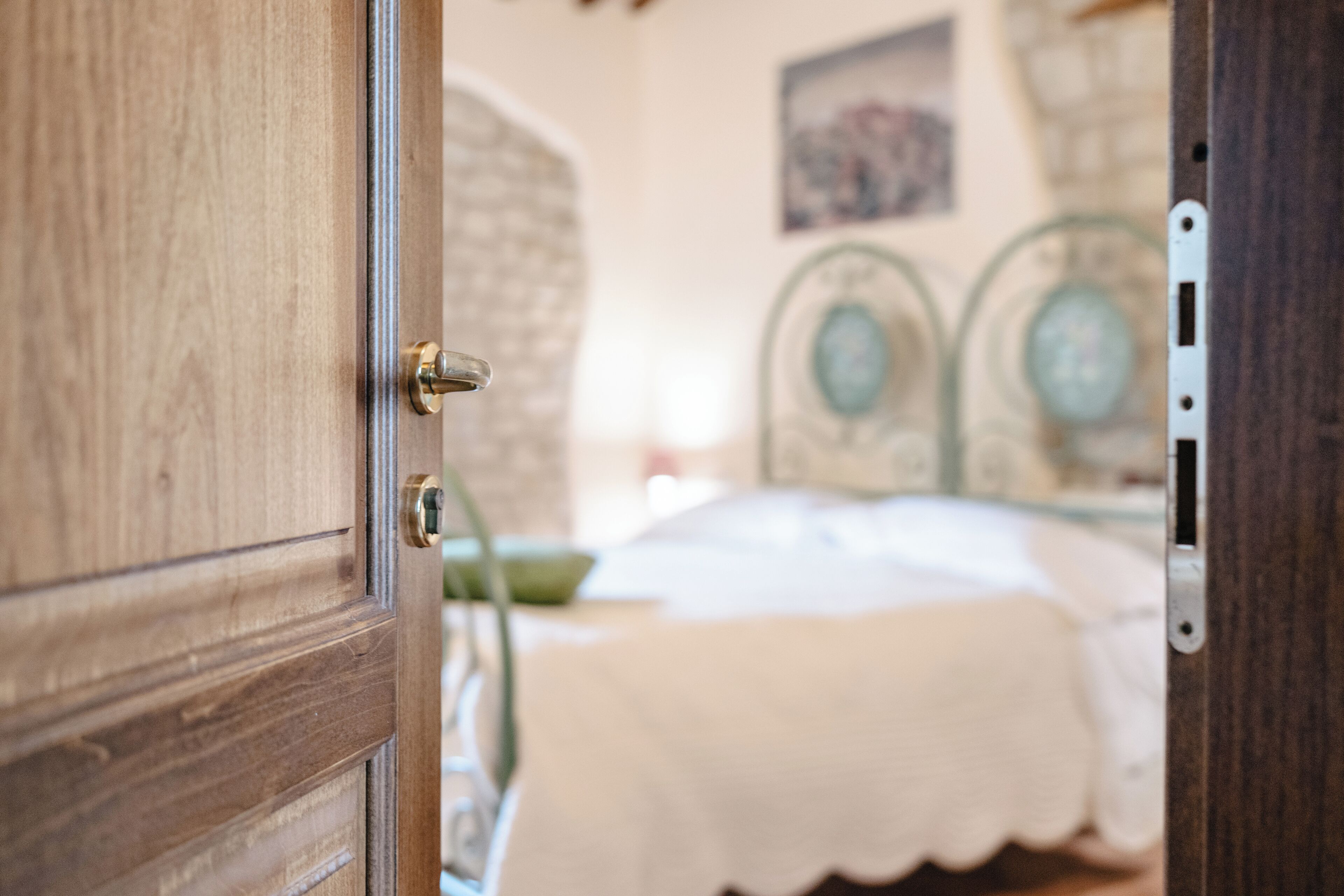 Une porte en bois dotée d’une poignée en laiton s’ouvre sur une pièce comprenant un lit, une tête de lit décorative en métal et un tableau accroché au mur.