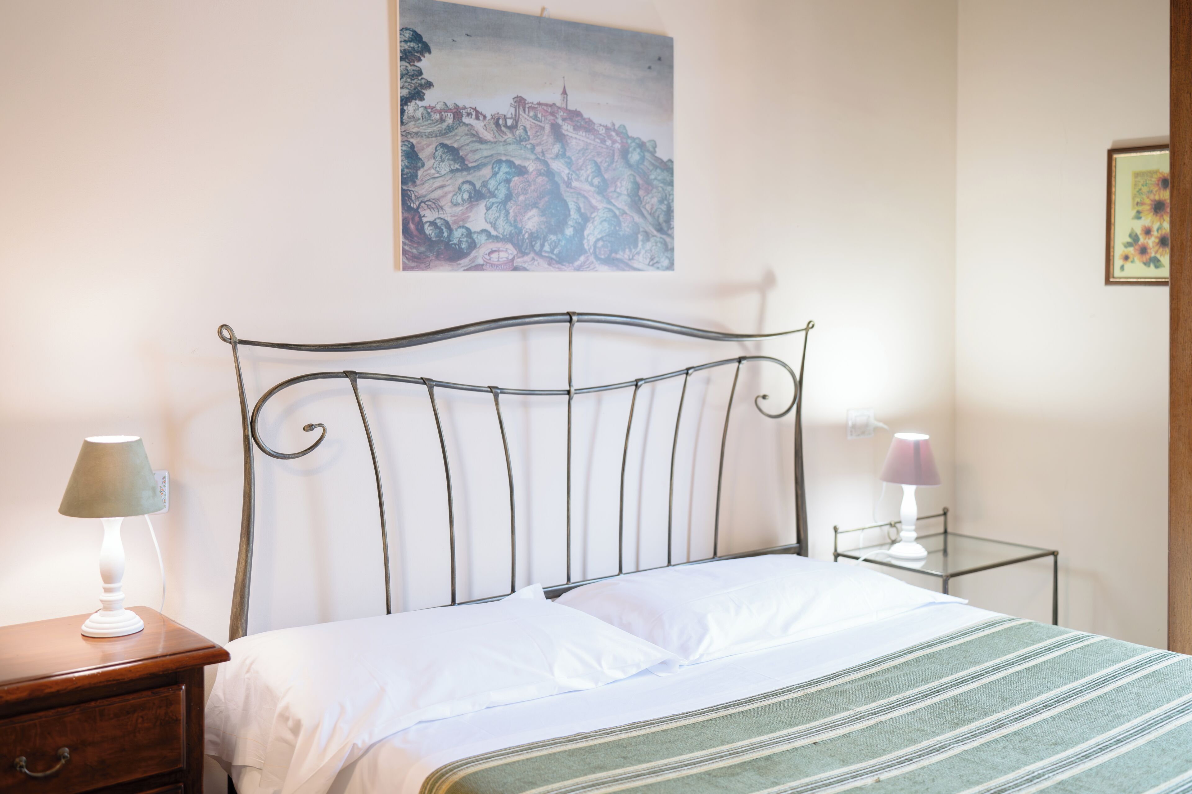 A bed with a metal headboard, a bedside table with a lamp, and a small bedside table with a lamp.