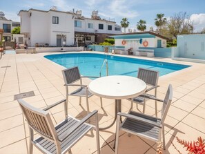 Une piscine avec des chaises longues et une table, entourée d’immeubles.
