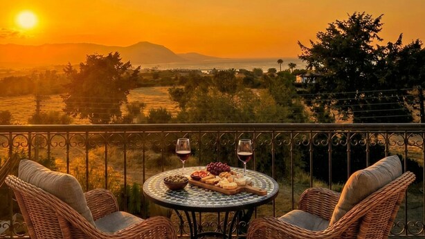 A balcony with wicker chairs, a round table with food and wine, and a sunset view. - Summer Haven, Polis: Sea & Mountain Views, Roof Terrace (Polis Chrysochous)