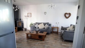 A modern living room with a grey sofa, a wooden coffee table, and a grey armchair. There is a small side table with a vase and a picture frame. The room has a wooden floor and white walls. - Summer Haven, Polis: Sea & Mountain Views, Roof Terrace (Polis Chrysochous)