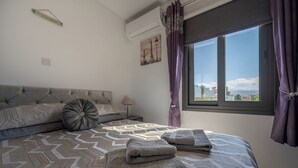A bedroom with a large bed, a view of the outdoors, and a window with purple curtains. - Summer Haven, Polis: Sea & Mountain Views, Roof Terrace (Polis Chrysochous)