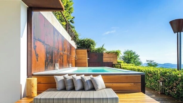 A modern outdoor seating area with a pool, wooden deck, and a view of the landscape. - House on the Langhe - Luxury private Pool, Sauna and Jacuzzi (Diano D'alba)