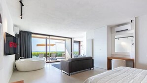 A modern hotel room with a large bed, a flat-screen TV, a built-in bathtub, and a balcony with a view. - House on the Langhe - Luxury private Pool, Sauna and Jacuzzi (Diano D'alba)