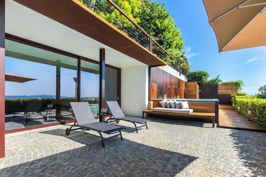 A modern outdoor patio with lounge chairs, a wooden bench, and a view of the ocean.