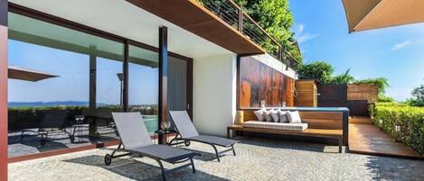 A modern outdoor patio with lounge chairs, a wooden bench, and a view of the ocean.