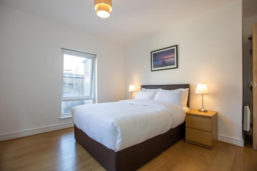A bedroom with a bed, bedside lamps, a window, and a framed picture on the wall.