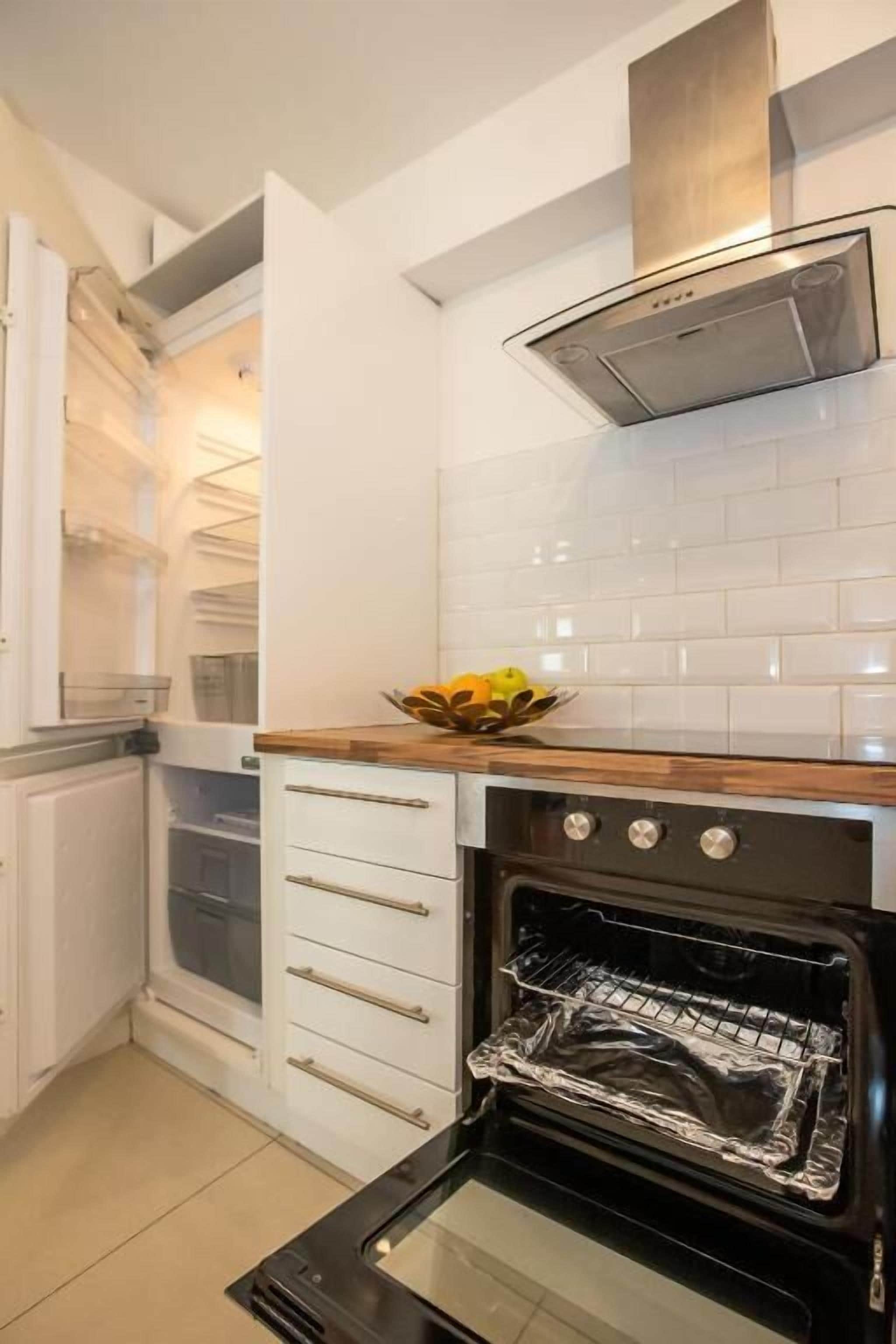 Una cocina con horno empotrado, campana extractora de acero inoxidable y salpicadero de azulejos blancos.