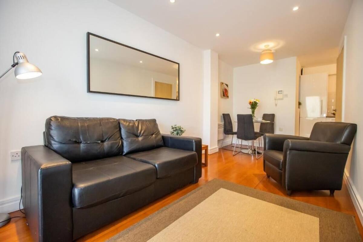 Een moderne woonkamer met een zwarte leren bank, een eettafel met stoelen en een grote spiegel aan de muur.