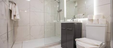 Un baño moderno con ducha de vidrio, inodoro y tocador con espejo.