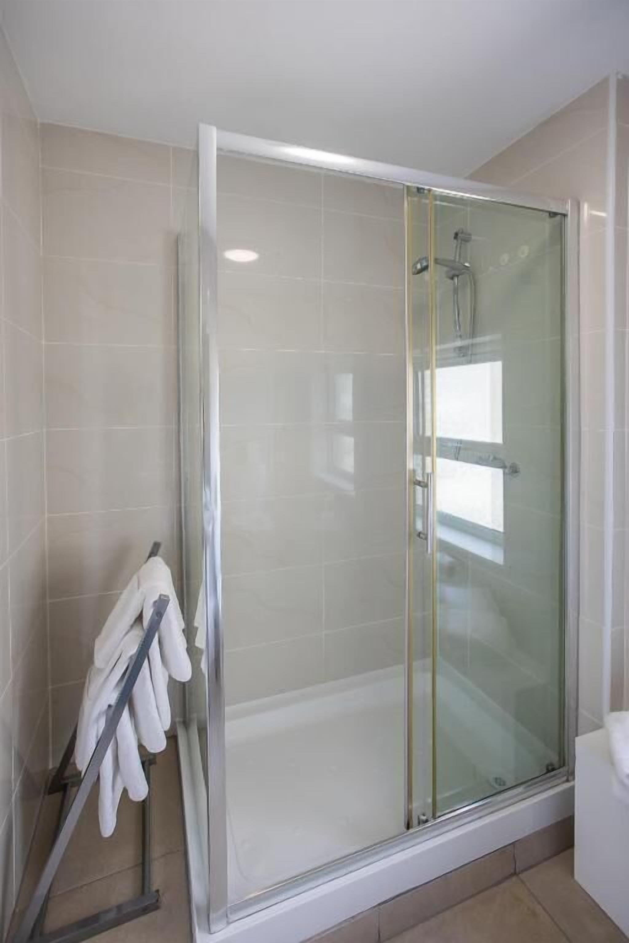 A glass-enclosed shower with a white tiled wall and a towel rack with white towels.