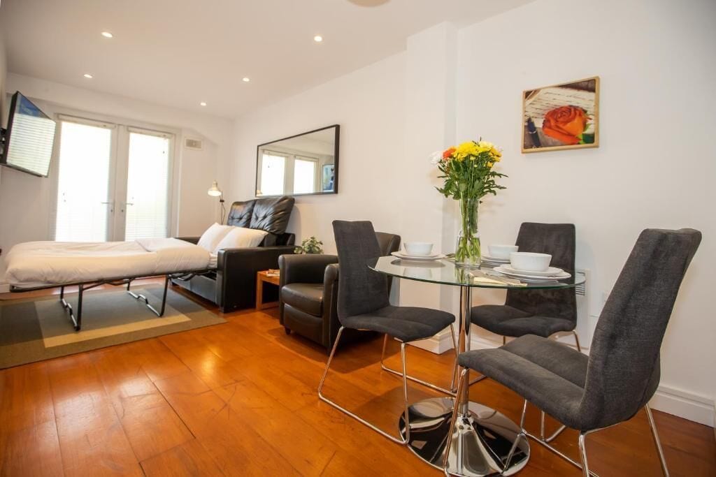 Une chambre d’hôtel moderne comprenant un lit, un canapé, une table à manger avec des chaises et un vase avec des fleurs.
