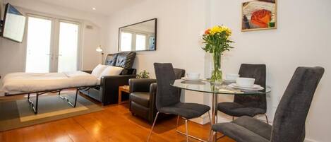 Une chambre d’hôtel moderne comprenant un lit, un canapé, une table à manger avec des chaises et un vase avec des fleurs.