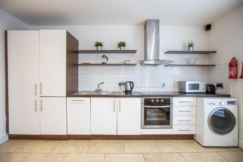Uma cozinha moderna com armários brancos, um exaustor de aço inoxidável, micro-ondas, forno e máquina de lavar.