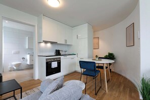 A compact kitchen with white cabinets, a built-in oven, and a dining area with a table and chairs. - Studio Multertor with Parking lot (St. Gallen)