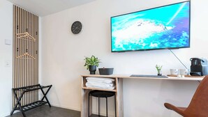 A modern room with a desk, a chair, a TV, a clock, a plant, and a hanging coat rack. - Central St. Gallen Studio (yellow): Fast WiFi & kitchen for shared use (St. Gallen)
