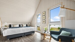 A bedroom with a large bed, a chair, a small table, and a view of the outside.