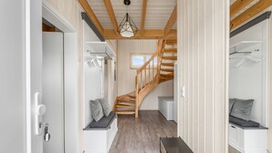 A narrow hallway with a wooden staircase leading to a loft bedroom. There are two seating areas with cushions, a radiator, and a hanging light fixture.