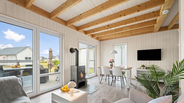 A spacious living area with a large sliding glass door leading to a balcony, a fireplace, a dining area, and a television mounted on the wall.