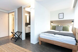 A modern bedroom with a wooden bed, a chair, and a bathroom visible through an open door. - Central St. Gallen Studio (red): Fast WiFi & kitchen for shared use (St. Gallen)
