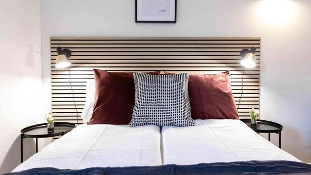 A bed with a headboard, two bedside tables, a framed picture, and a wall-mounted light fixture. - Central St. Gallen Studio (blue): Fast WiFi & kitchen for shared use (St. Gallen)