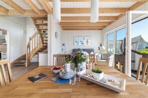 A dining area with a wooden table set for a meal, a staircase, and a view of the outside. - Kiek Inn - Infrared sauna, fireplace, bathtub, terrace, beach chair, parking (Olpenitz)