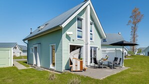 A two-story house with a covered patio, a small garden, and a clear sky. - Kiek Inn - Infrared sauna, fireplace, bathtub, terrace, beach chair, parking (Olpenitz)