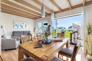 A spacious living area with a wooden dining table, grey sofa, and a painting of sailboats. - Kiek Inn - Infrared sauna, fireplace, bathtub, terrace, beach chair, parking (Olpenitz)