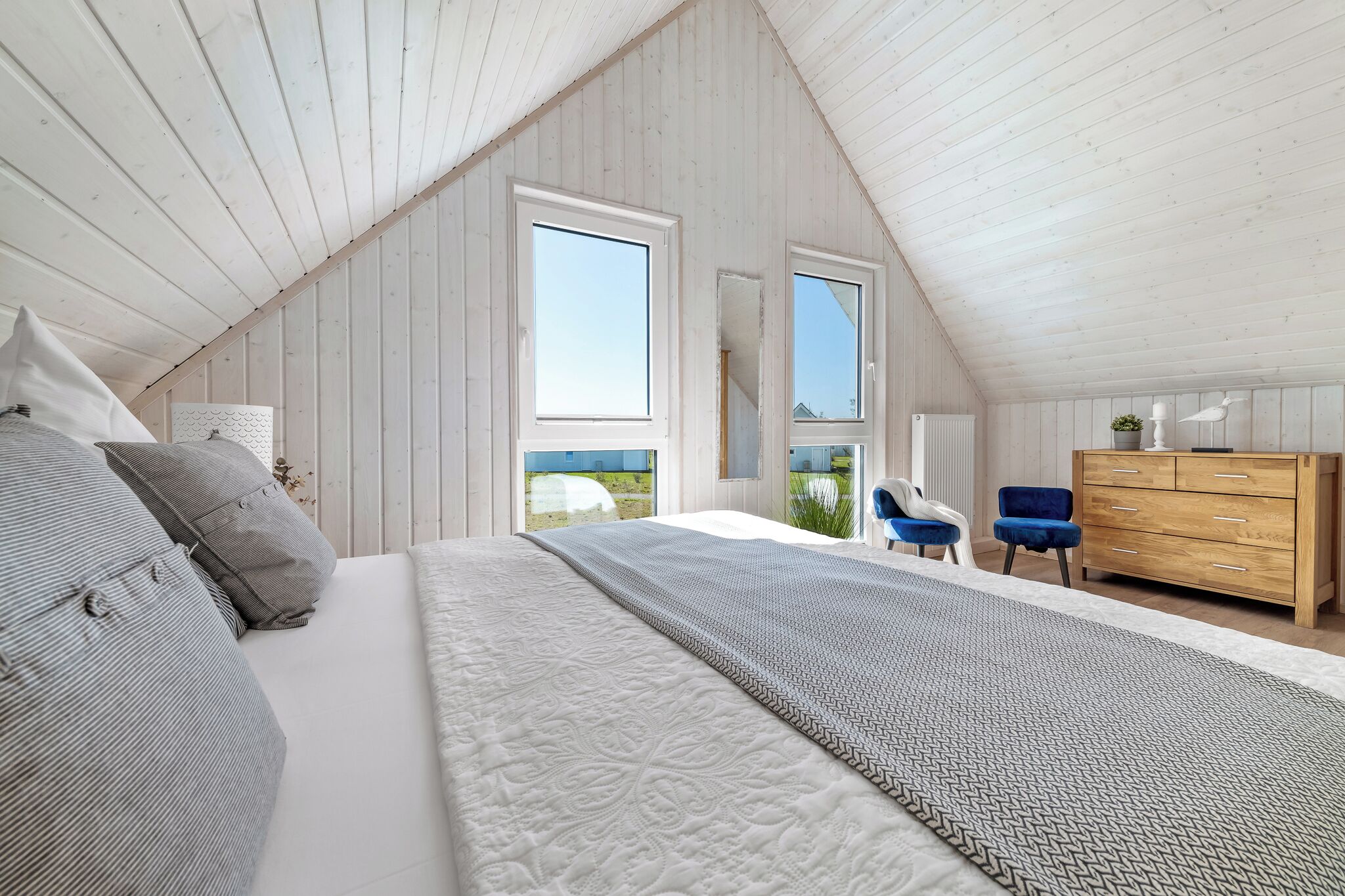 A bedroom with a sloped ceiling, a bed with patterned bedding, a dresser, and two chairs.
