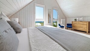 A bedroom with a sloped ceiling, a bed with patterned bedding, a dresser, and two chairs. - Kiek Inn - Infrared sauna, fireplace, bathtub, terrace, beach chair, parking (Olpenitz)