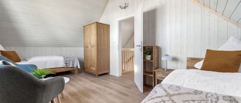 A cozy bedroom with two beds, a wooden wardrobe, a desk, and a chair.