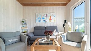 A modern living room with a sofa set, a coffee table, and a painting of sailboats on the wall. - Kiek Inn - Infrared sauna, fireplace, bathtub, terrace, beach chair, parking (Olpenitz)