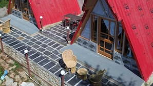 A model of a chalet with two red-roofed cabins, stone flooring, and wicker furniture. - Eva Cabins (Dalhousie)